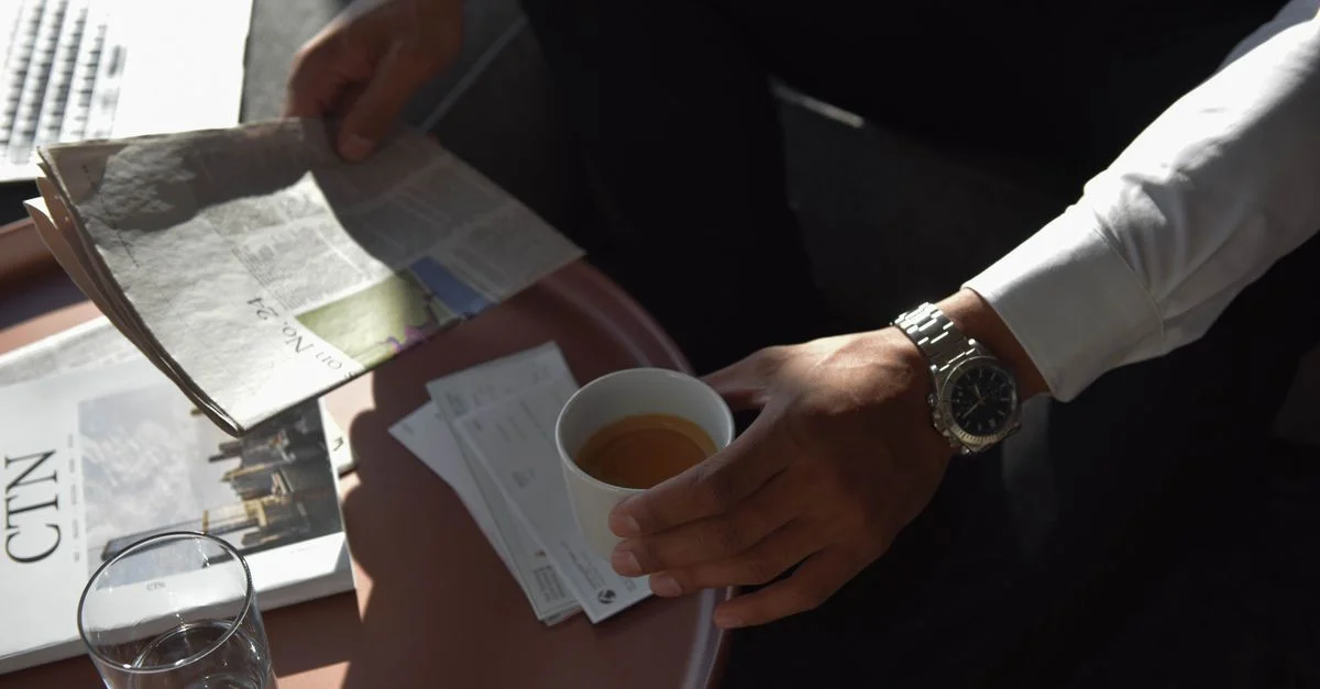 Homme d'affaires tenant une tasse de café et lisant un journal dans un cadre de bureau moderne.