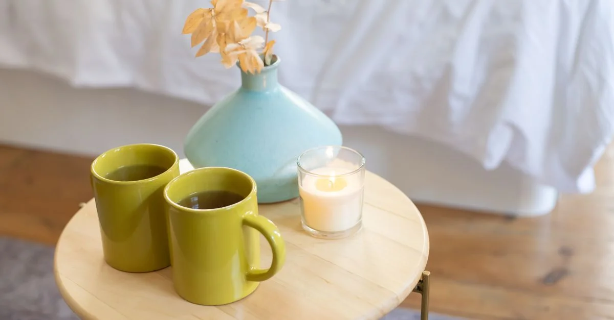 Une scène intérieure confortable avec des tasses vertes, une bougie allumée et un vase sur une table en bois.