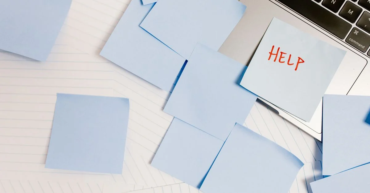 Un espace de travail encombré avec des Post-it sur un ordinateur portable, symbolisant la surcharge et le besoin d'aide.