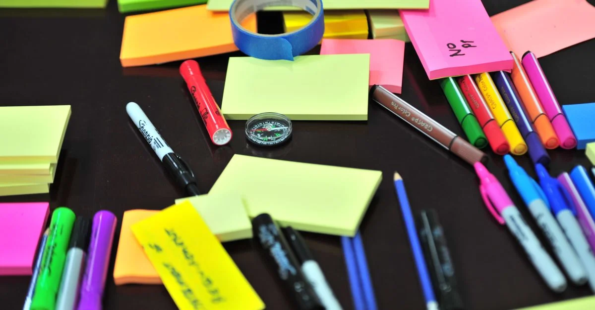 Assortiment coloré de fournitures de bureau sur un bureau, y compris des Post-it, des stylos et des marqueurs.