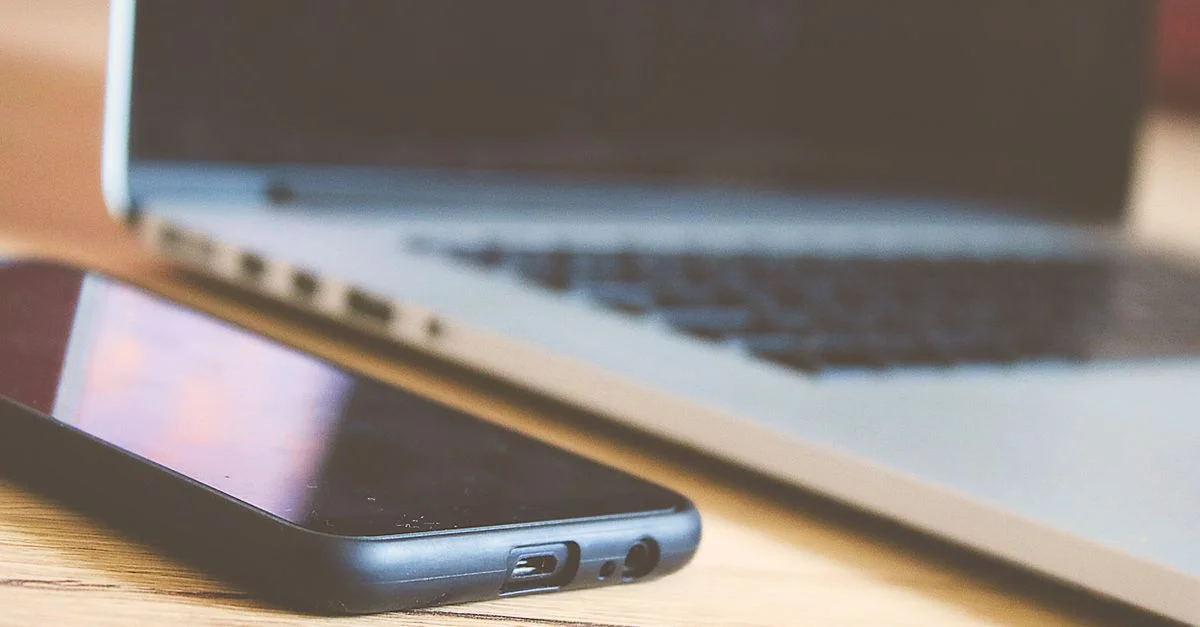 Vue en gros plan d'un smartphone et d'un ordinateur portable sur un bureau en bois, parfait pour illustrer la technologie moderne.