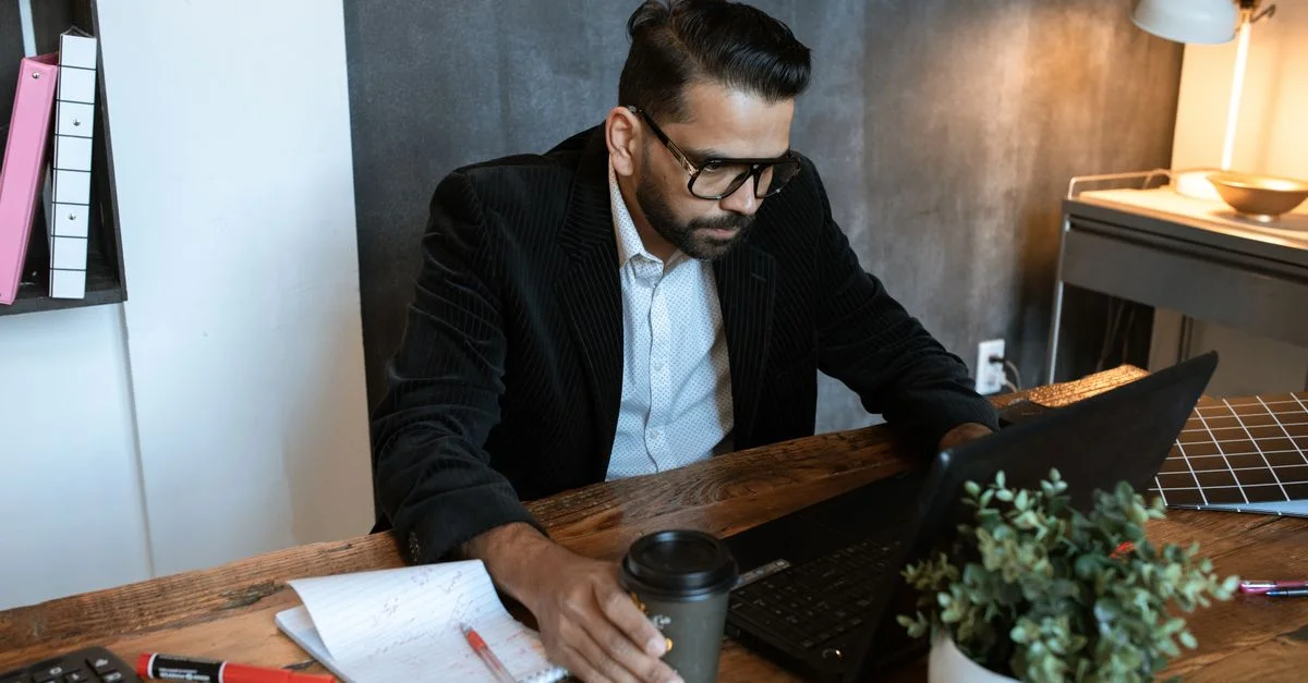 Homme concentré sur son ordinateur portable dans un bureau moderne, un café à la main.