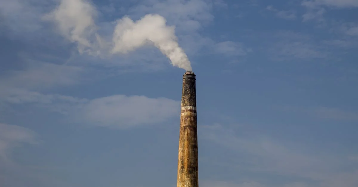 Une cheminée d'usine émettant de la fumée contre un ciel bleu dégagé, soulignant la pollution de l'air.